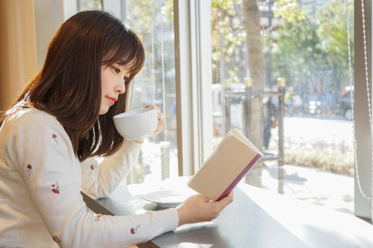 お茶をしながら読書を楽しむ女性の画像
